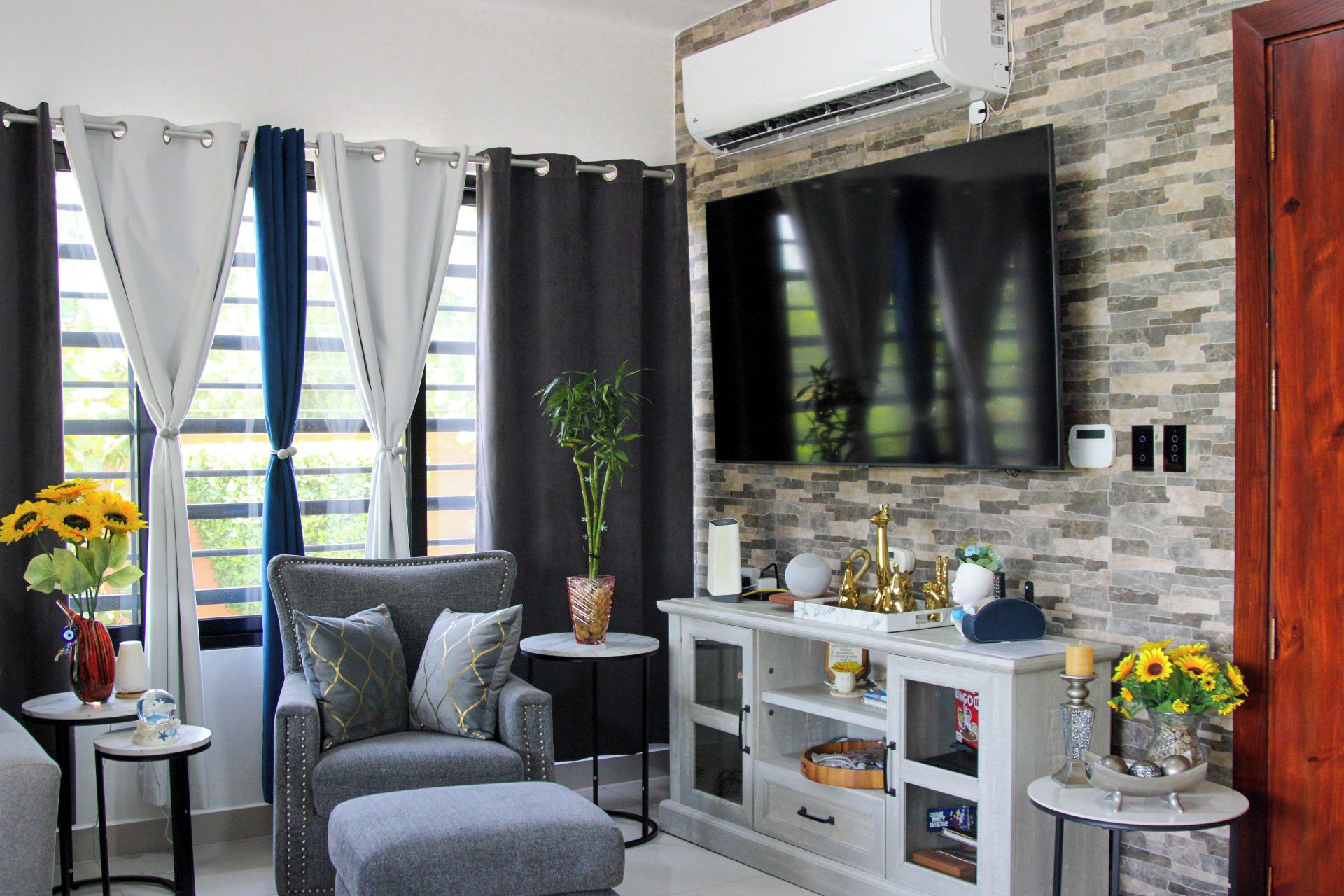 A living room with a grey sofa, a white cabinet, a flat-screen TV, and a window with curtains.