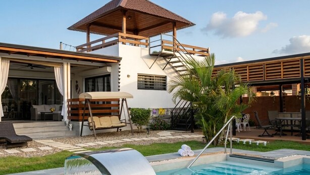 A pool area with a wooden deck, a covered seating area, and a staircase leading to a balcony.