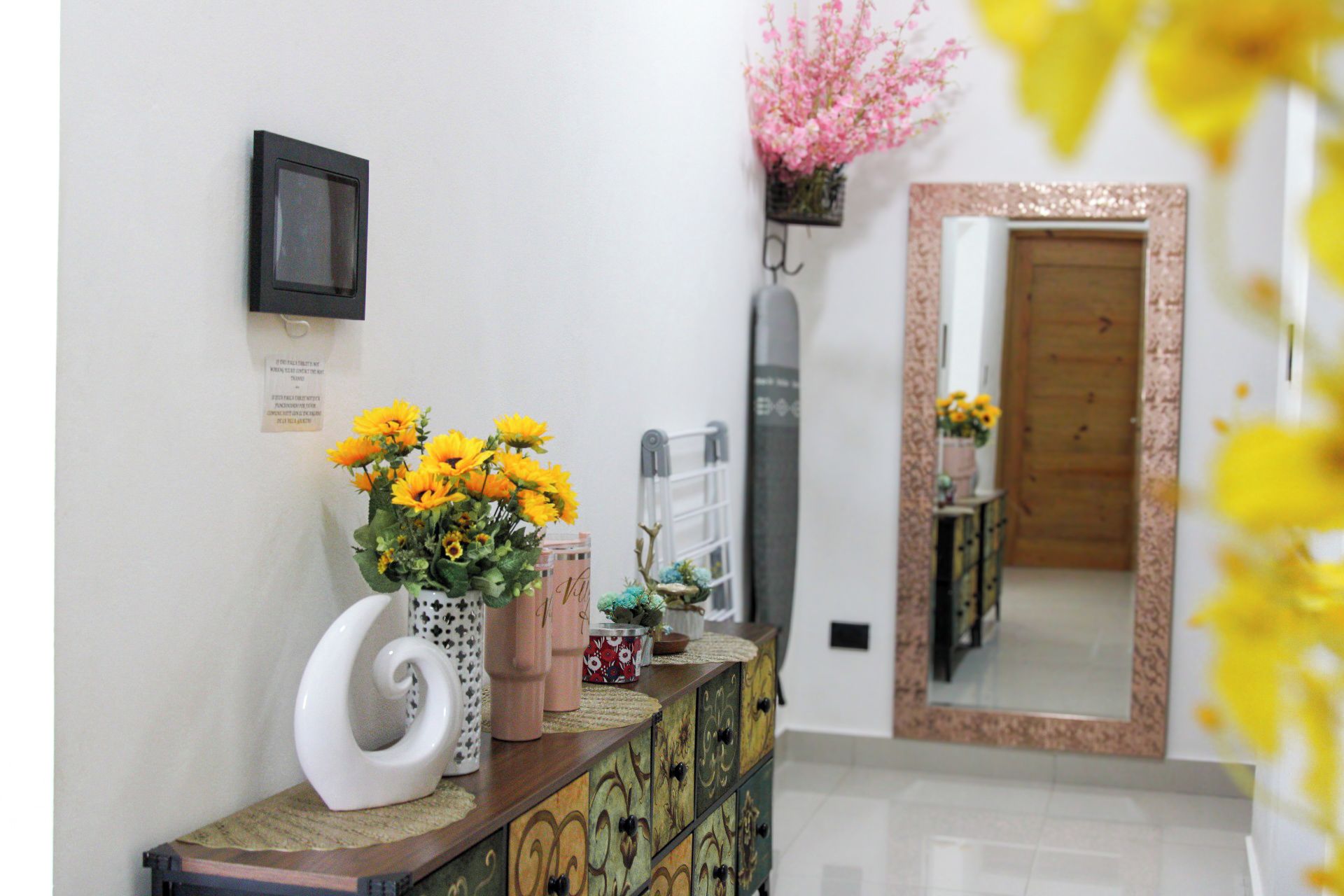 A reception area with a desk, a mirror, a wall-mounted TV, and a door leading to another room.