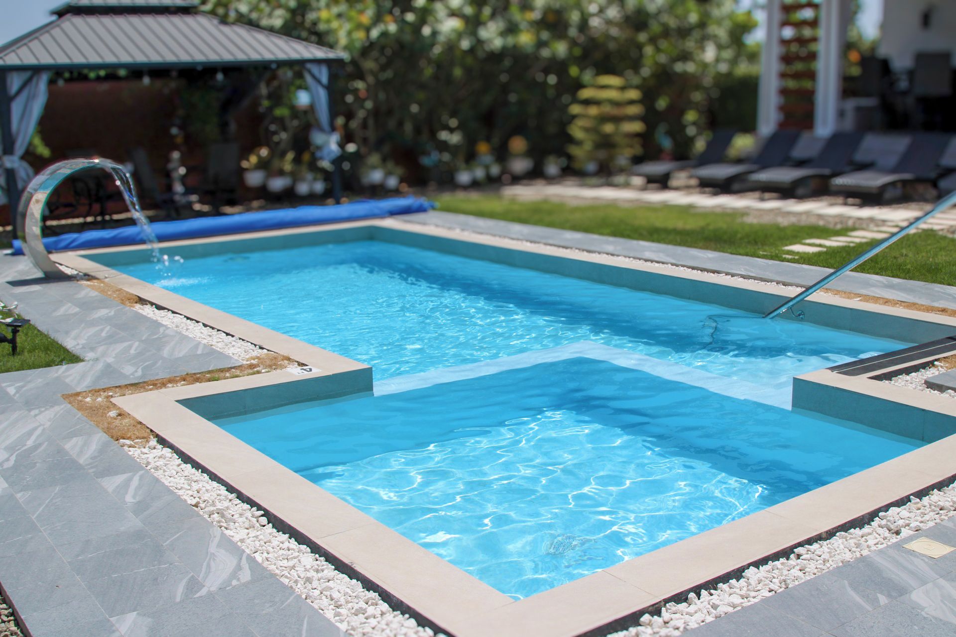 A rectangular swimming pool with a clear blue water surface, surrounded by a tiled deck with a pebble border.