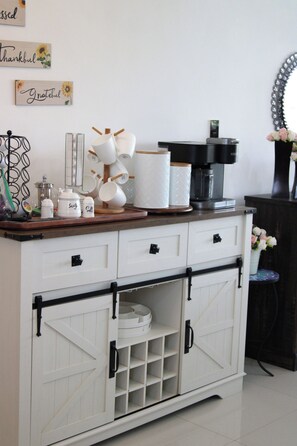 Una encimera de cocina con una cafetera, recipientes de azúcar y sal, y un escurre mugs.