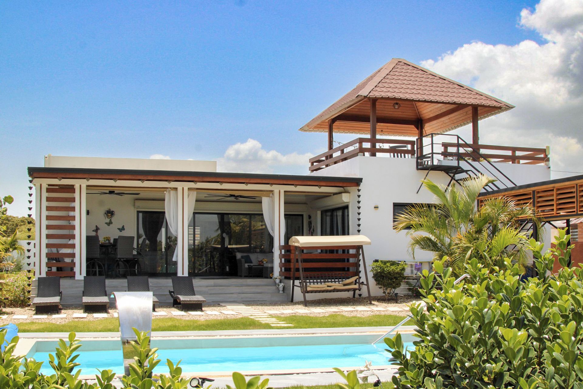 Una casa moderna con piscina, mobiliario exterior y terraza cubierta.