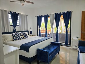 Een slaapkamer met een bed, nachtkastjes, een bankje en uitzicht op het omliggende landschap.