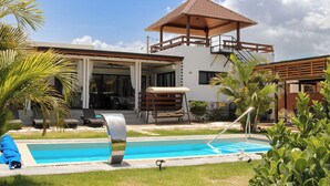 A modern house with a swimming pool, a covered patio, and a view of the sky.