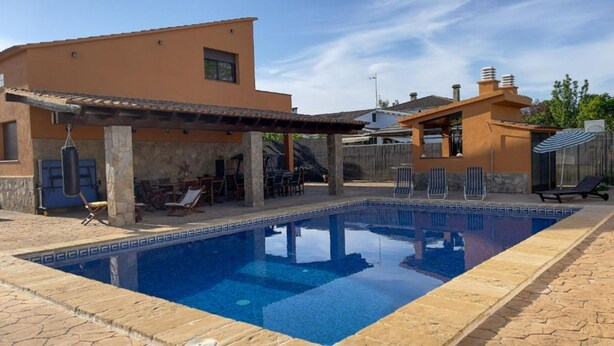 A swimming pool with a tiled deck, a covered patio area, and a small outdoor seating area with chairs and a table. - Martina House (Sant Julià d'Alfou)
