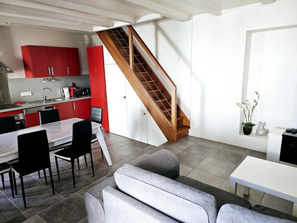 Une cuisine moderne avec des meubles rouges, un escalier en bois et un coin repas avec des canapés gris.