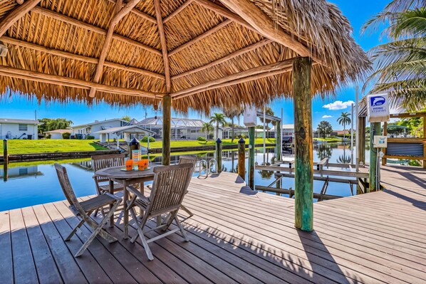 A wooden deck with a thatched roof pavilion, overlooking a calm water body and a golf course.