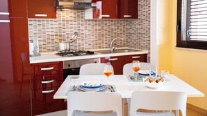 Une cuisine moderne avec des meubles rouges, un plan de travail blanc et un coin repas comprenant une table et des chaises blanches.