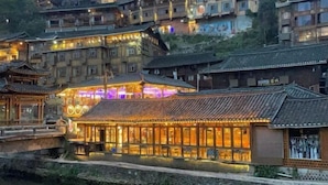 A traditional building with a tiled roof and a stone foundation, adjacent to a body of water. - Xijiang Anxia B&B (Leishan)