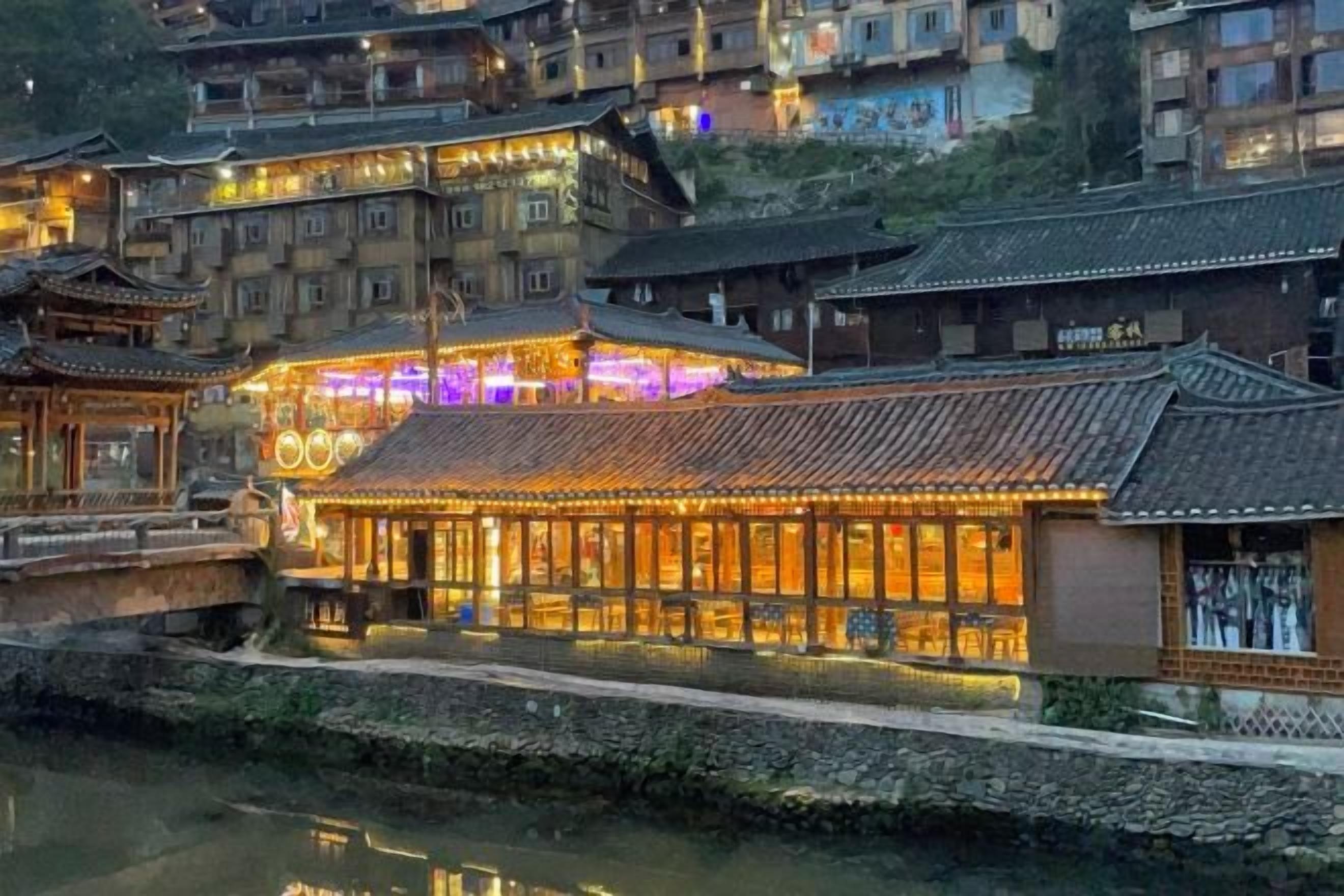 A traditional building with multiple levels, a river in the foreground, and a well-lit facade.