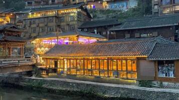 A traditional building with multiple levels, a river in the foreground, and a well-lit facade.