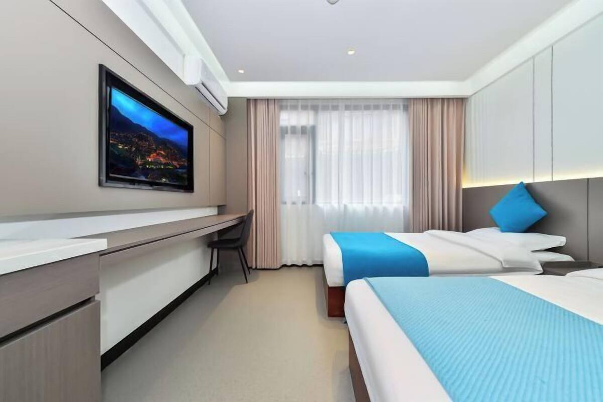 A hotel room with a bed, a desk, a television, and a window with curtains.