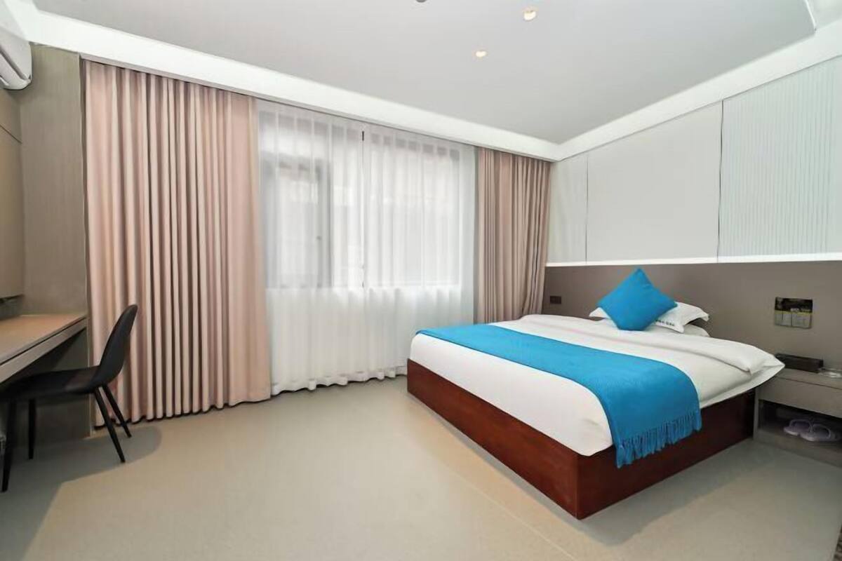 A hotel room with a bed, a desk, a chair, and a window with curtains.