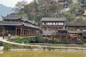 A traditional Chinese courtyard with wooden buildings, a pond, and a stone bridge.