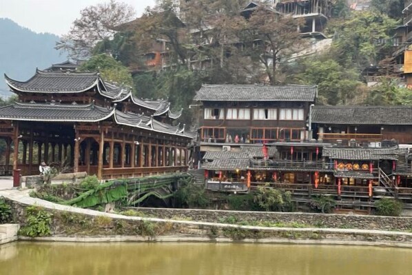 A traditional Chinese courtyard with wooden buildings, a pond, and a stone bridge.