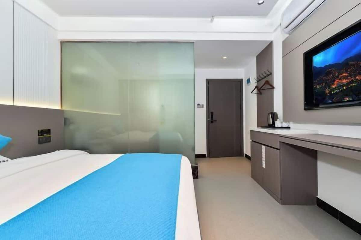 A hotel room with a bed, a TV, a desk, and a door.