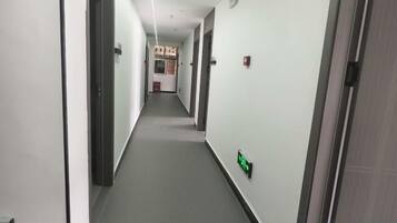 A narrow hallway with doors on both sides, a fire alarm on the right wall, and a light switch on the left wall.