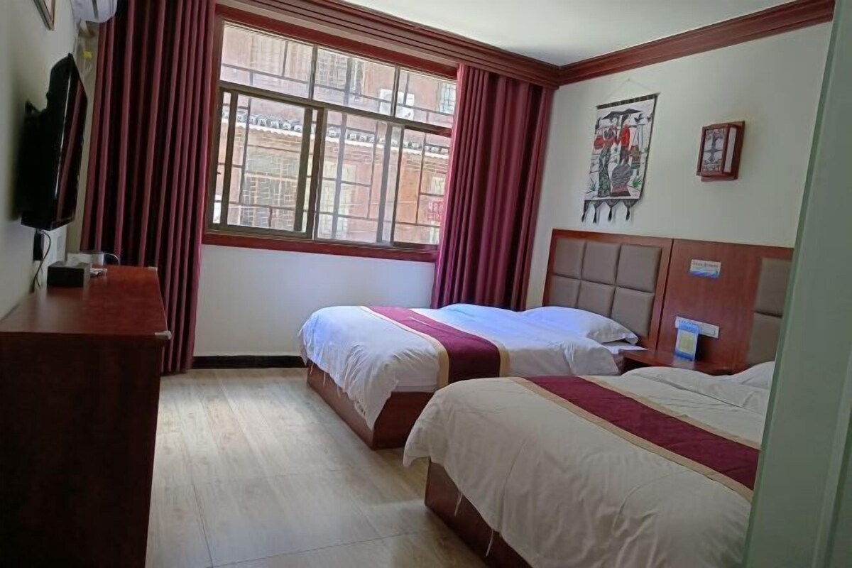 Quarto de hotel com duas camas, uma escrivaninha de madeira, uma janela com cortinas e obras de arte na parede.