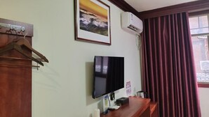 A room with a wooden desk, a mounted TV, an air conditioner, a framed picture, and a window with curtains. - Xijiang Anxia B&B (Leishan)