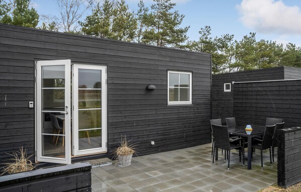Eine moderne Außenpatio mit einem dunklen Holzbau, einer Schiebetür aus Glas, einem kleinen Fenster und einem Tisch mit Stühlen.
