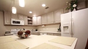 Una cocina con armarios blancos, microondas, refrigerador y un comedor con individuales.