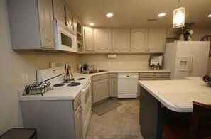 Kitchen features a central island with a stove, sink, and dishwasher, along with a kettle on the countertop.