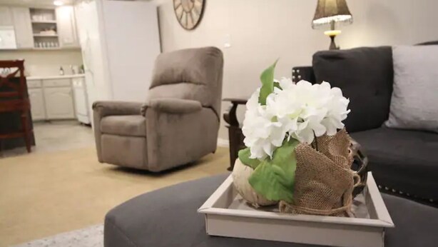 Una sala de estar con un sofá gris, una mesita con un arreglo floral blanco y una lámpara.