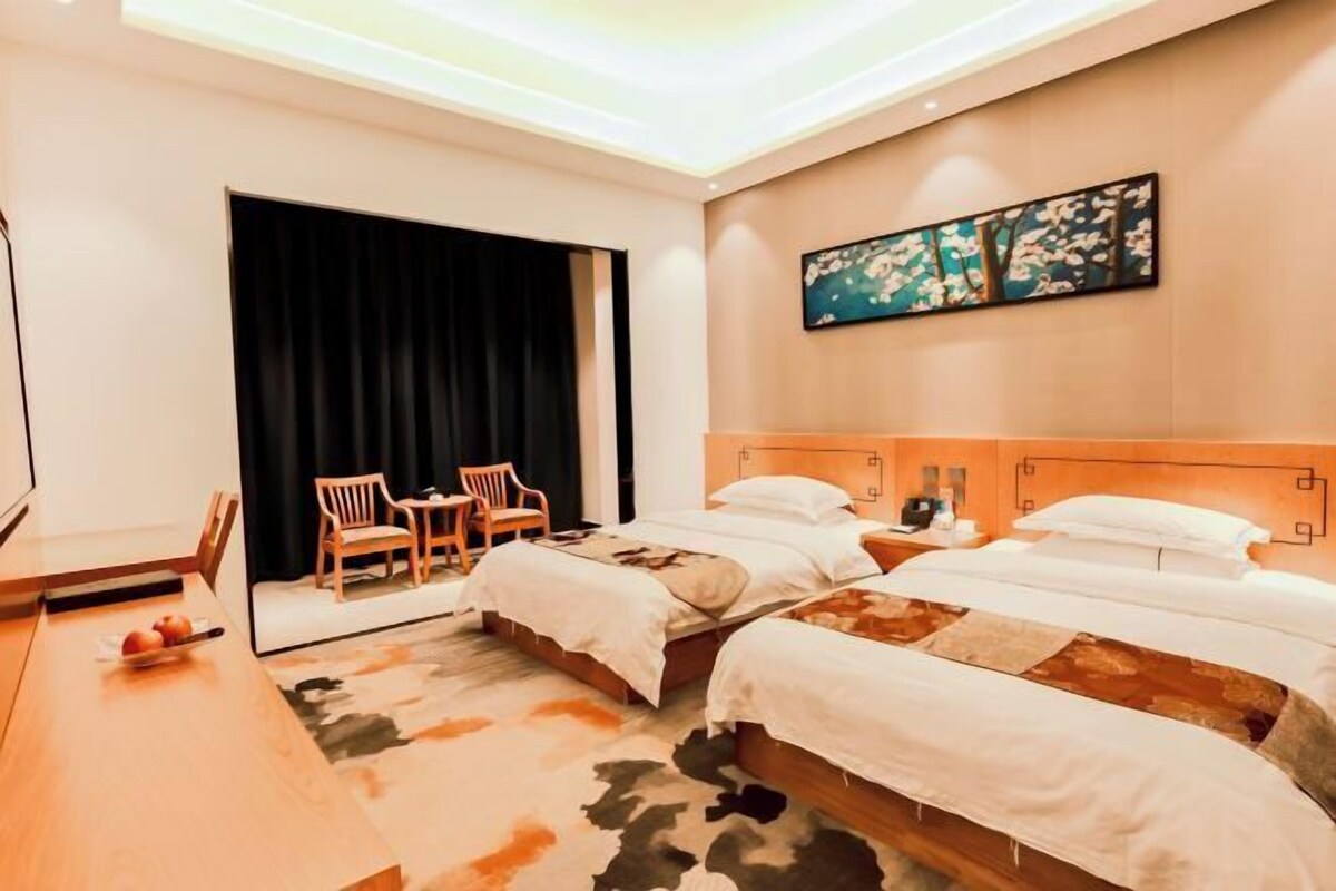 A hotel room with two beds, a large window, a painting on the wall, and a wooden chair.
