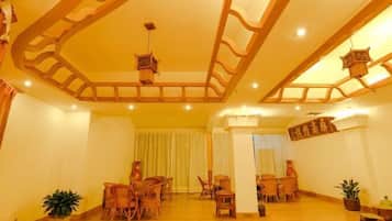 A spacious room with wooden flooring, multiple seating areas, and a high ceiling with decorative wooden beams.