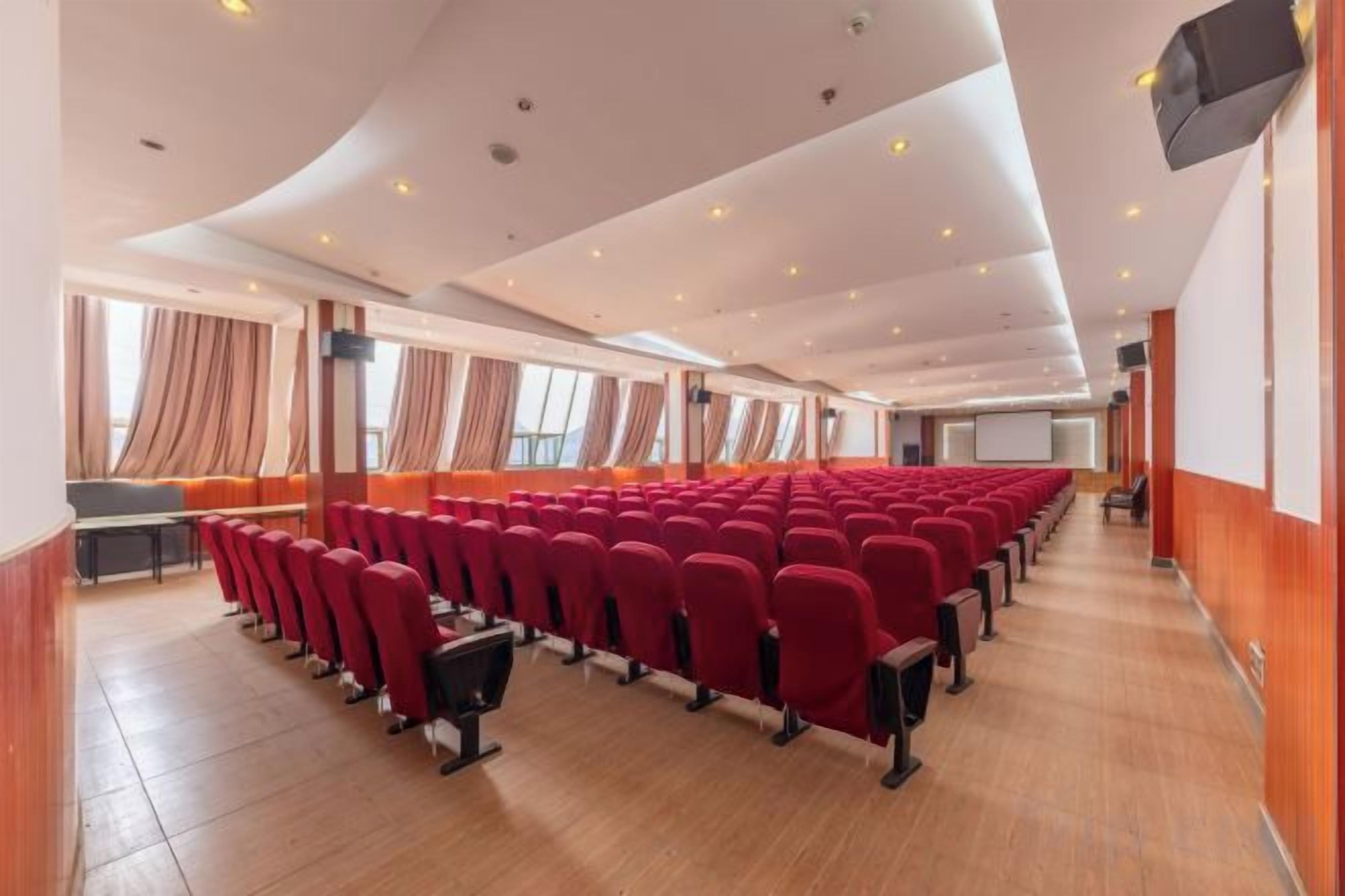 A theater with rows of red seats, a wooden floor, and a curved ceiling.