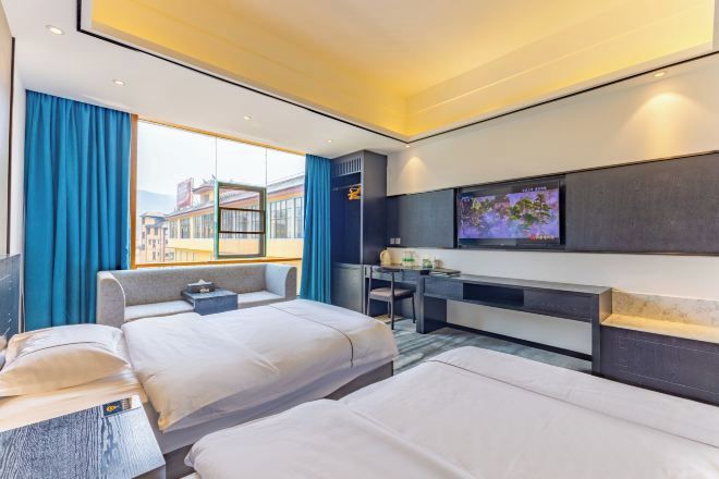 Habitación de hotel con dos camas, un escritorio, un televisor y un ventanal con cortinas.