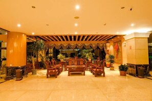 A lobby with a central wooden bench surrounded by chairs, potted plants, and a decorative ceiling. - Yunti Hotel (Lvchun)