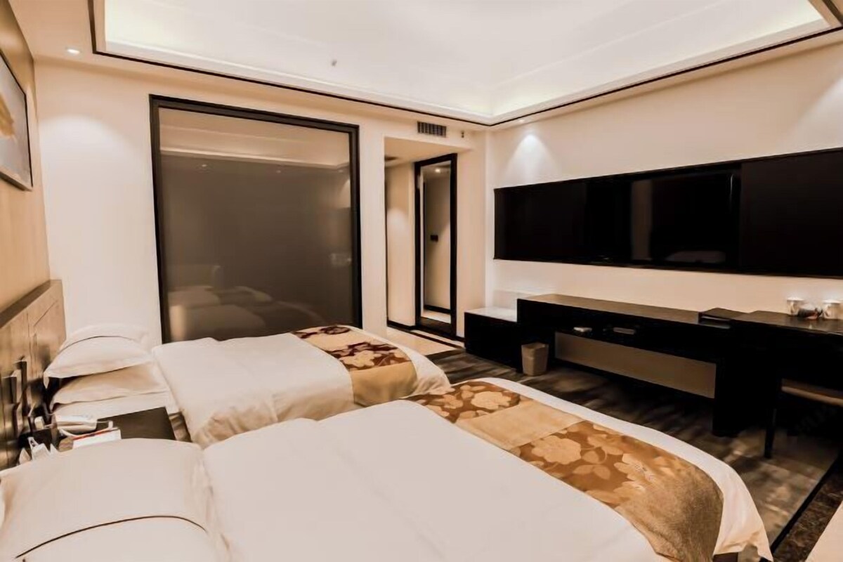 A hotel room with two beds, a desk, a flat-screen TV, and a sliding door leading to a bathroom.
