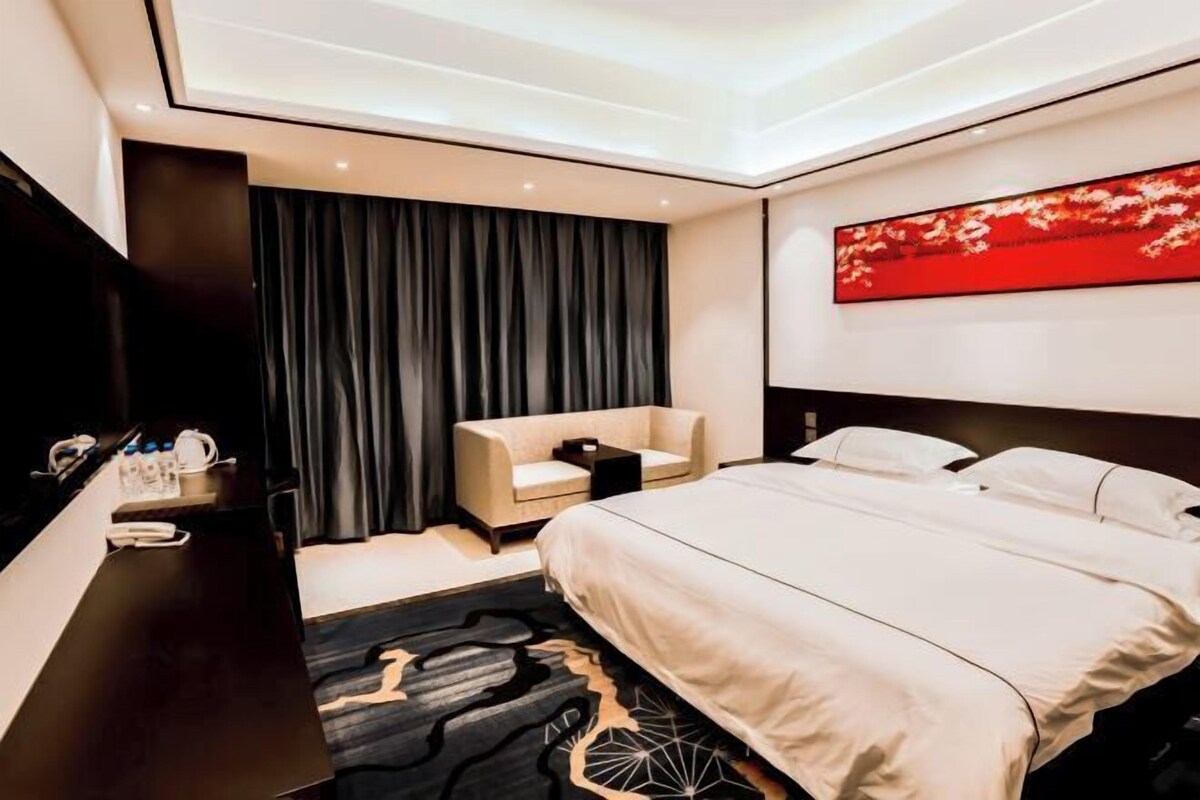 A modern hotel room with a bed, a desk, a chair, and a large window.