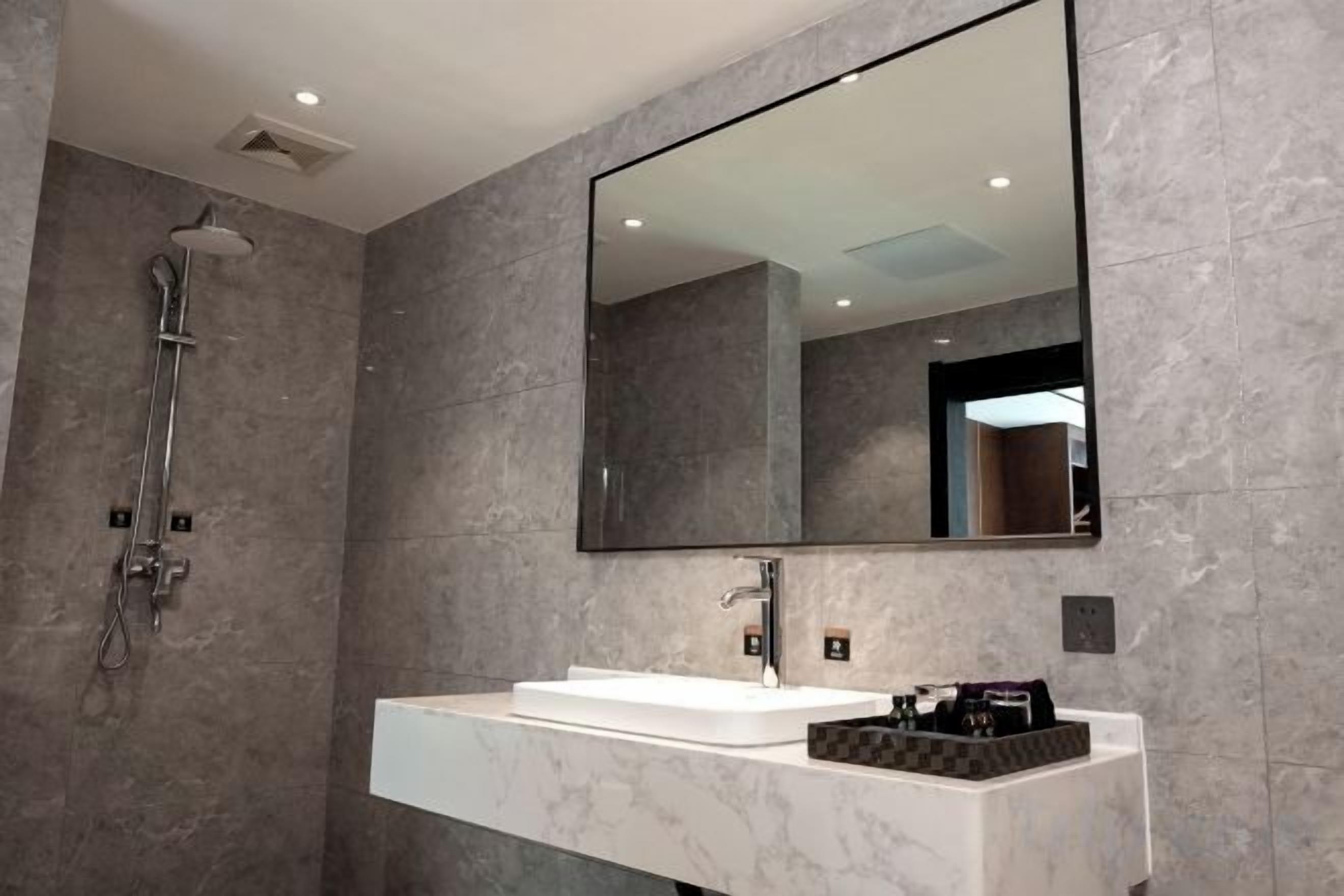 A modern bathroom with a large mirror, a shower, and a white sink.