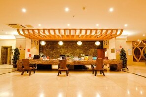 A reception area with a wooden reception desk, multiple chairs, and a stone wall backdrop. - Yunti Hotel (Lvchun)