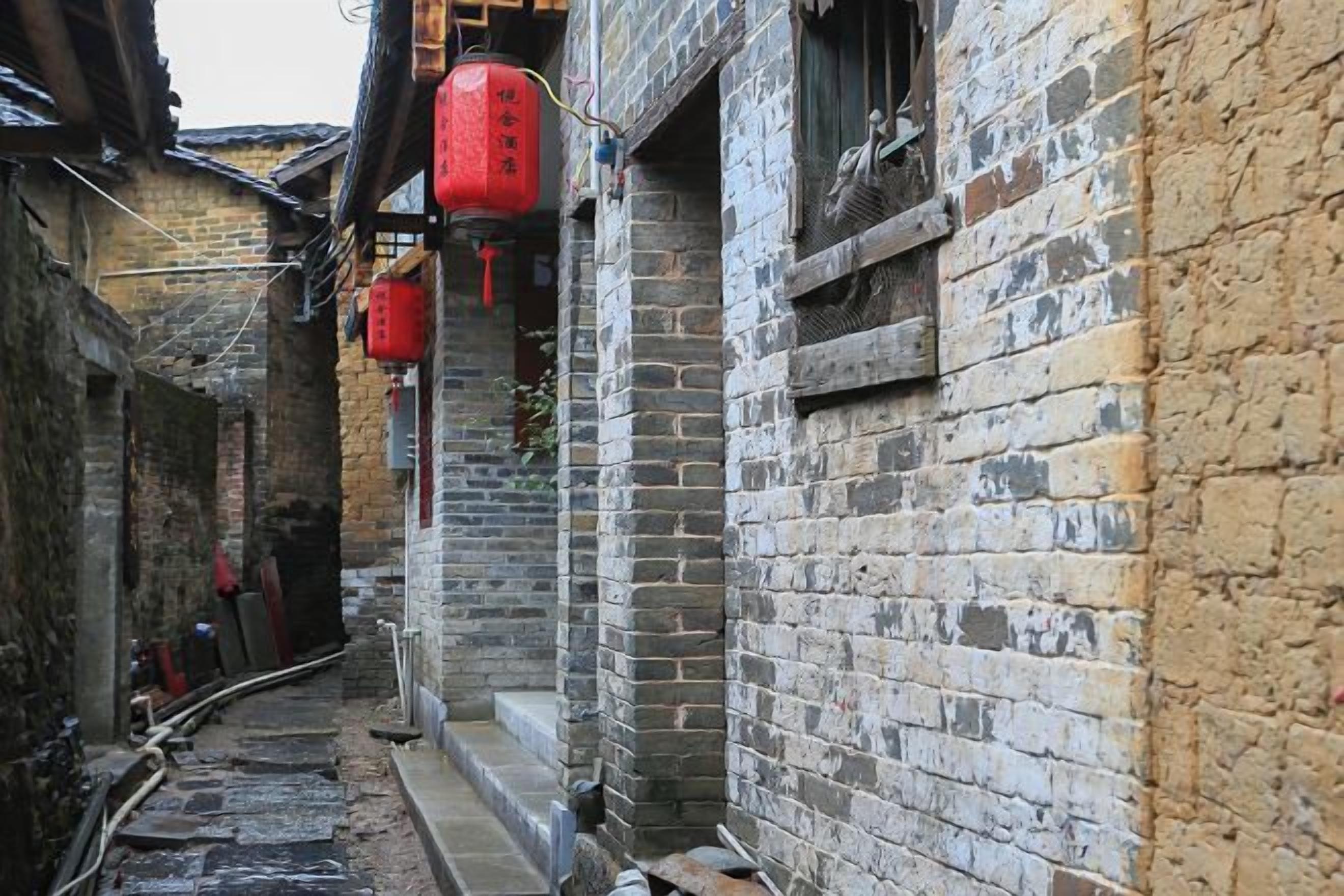 A narrow alleyway with traditional brick buildings, red lanterns, and a visible water pipe.