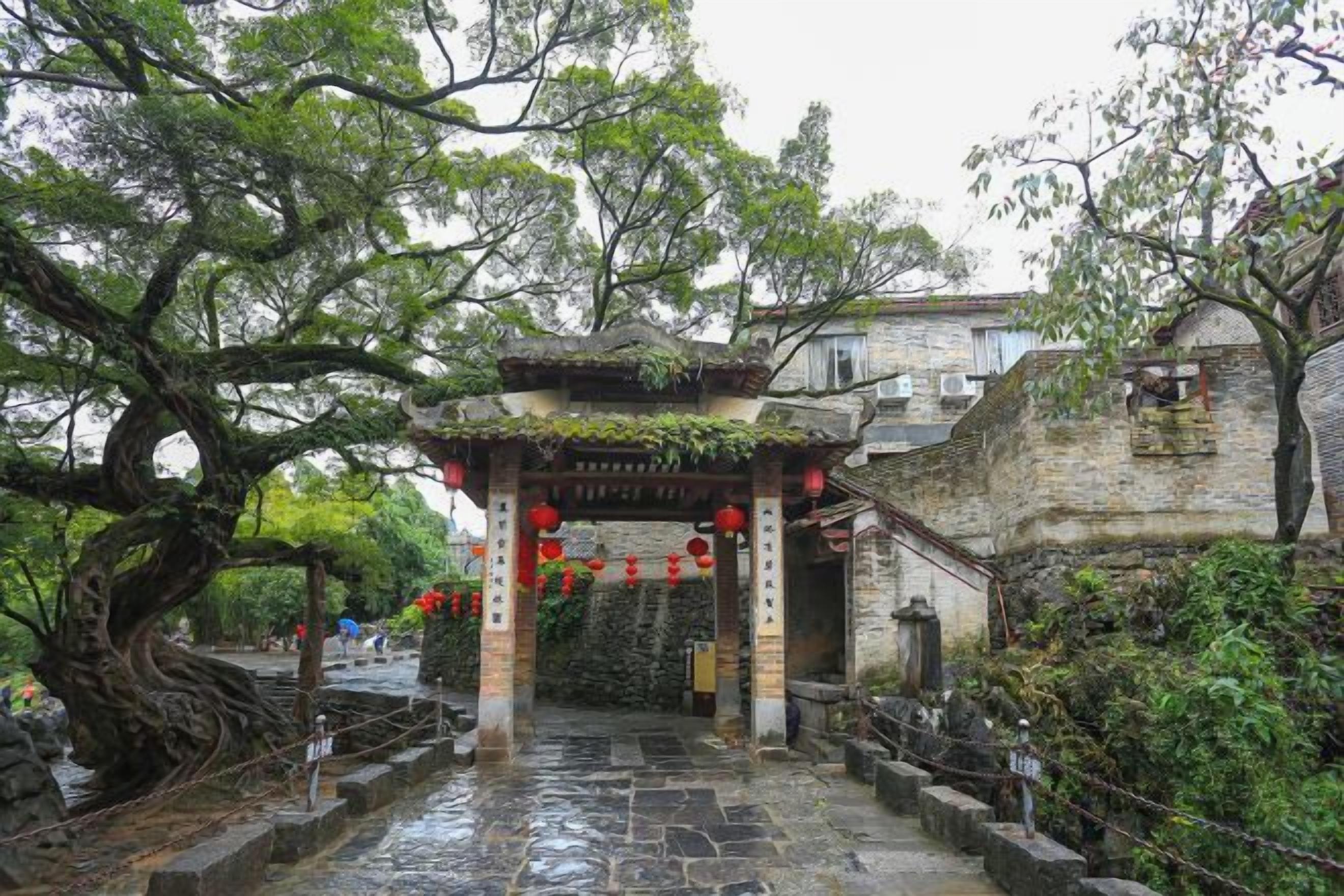 A traditional gate with a stone pathway leading through it, surrounded by trees and a stone wall.