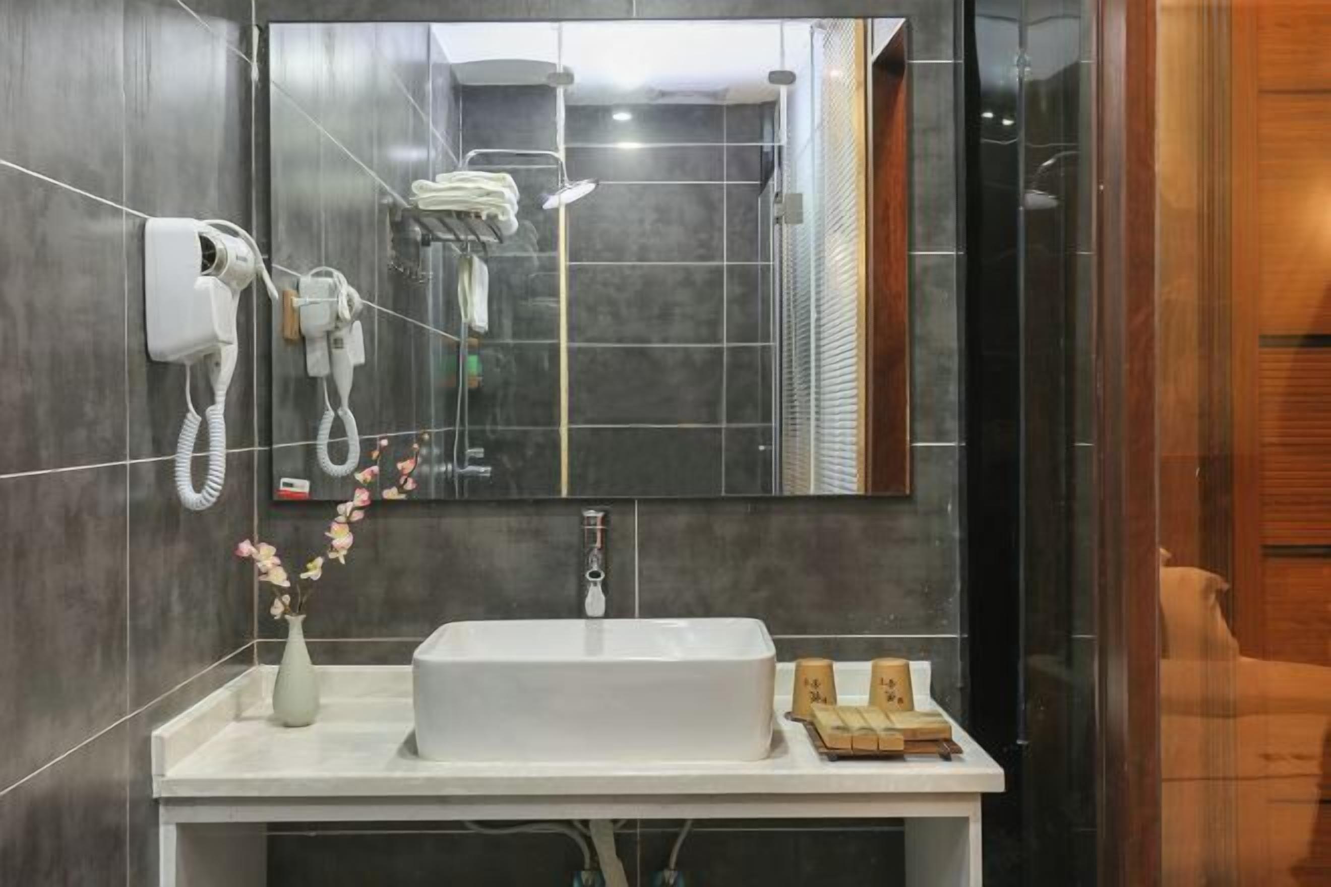 A modern bathroom with a large mirror, a white sink, a handheld showerhead, and a towel rack.