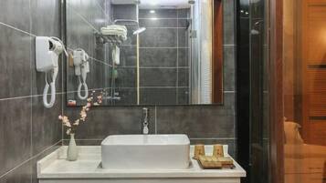 A modern bathroom with a large mirror, a white sink, a handheld showerhead, and a towel rack.