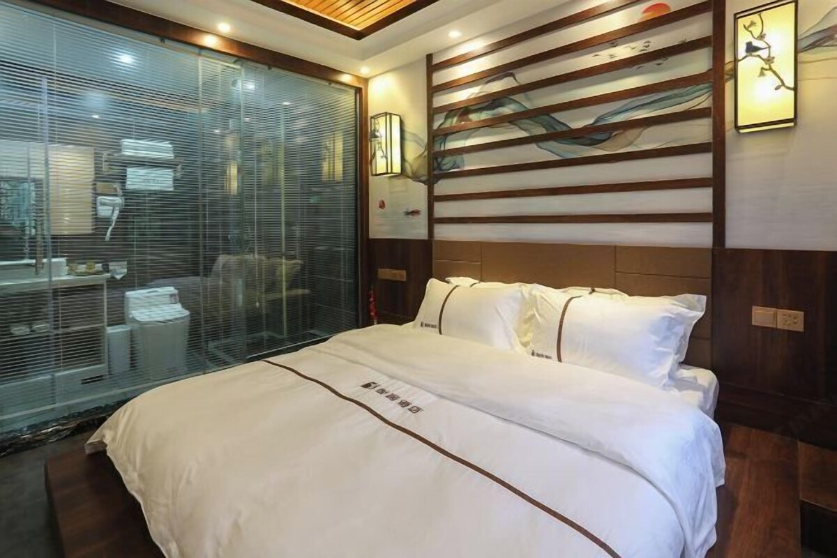 Habitación de hotel con una cama grande, un muro de cristal y un cabecero de madera con un cuadro.