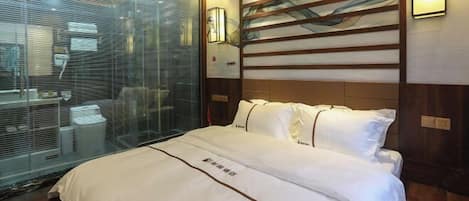 Quarto de hotel com uma cama grande, parede de vidro e cabeceira de madeira com uma pintura.