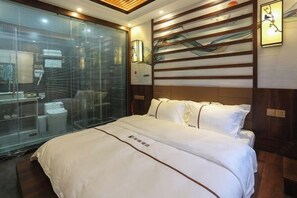 Habitación de hotel con una cama grande, un muro de cristal y un cabecero de madera con un cuadro.