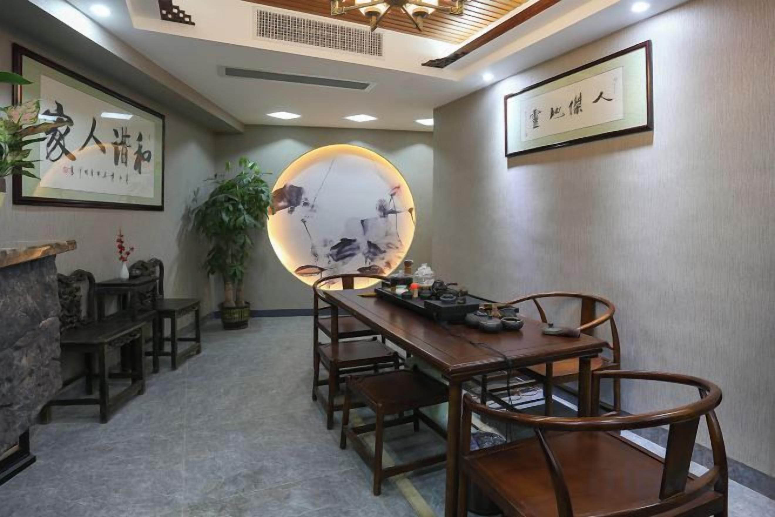 A traditional-style dining room with a long wooden table and chairs, a round table with a decorative centerpiece, and framed calligraphy on the walls.