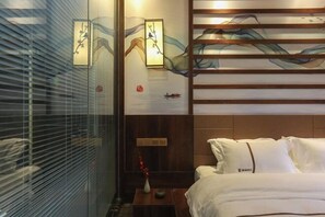 Habitación de hotel con cama, mesita de noche, reloj en la pared y ventana con persianas.