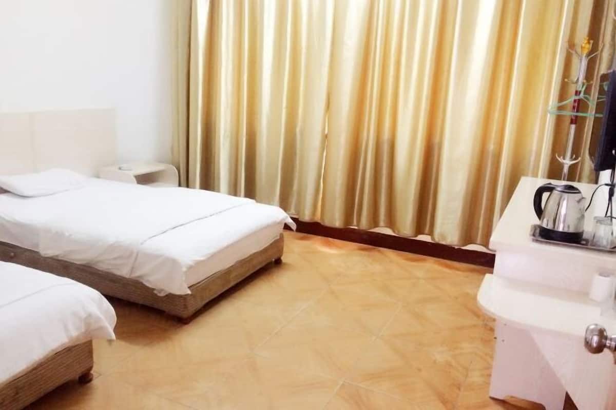 A hotel room with two beds, a bedside table, a nightstand, a coffee maker, and a curtain.