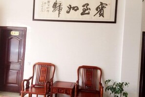 A room with a wooden door, two wooden chairs, a small table, and a framed calligraphy artwork on the wall. - Anping Hotel (Wuyishan)
