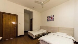 Una habitación de hotel con dos camas, piso de madera, ventilador de techo y una puerta.