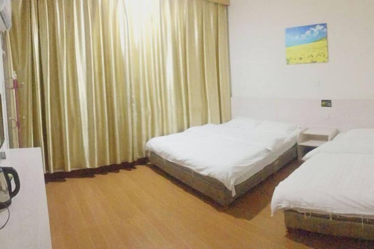 A hotel room with two single beds, a wooden floor, a curtain, and a painting on the wall.