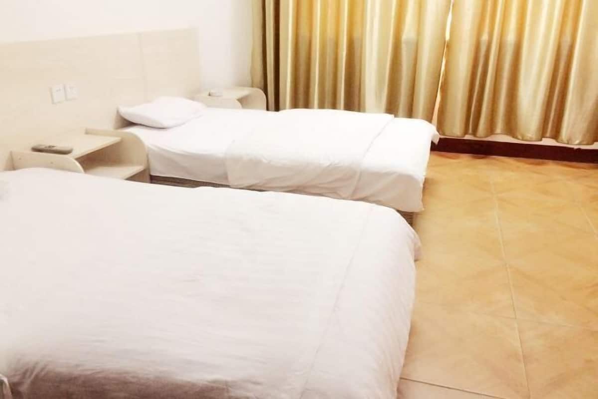 A hotel room with two beds, a bedside table with a lamp, and a curtain.